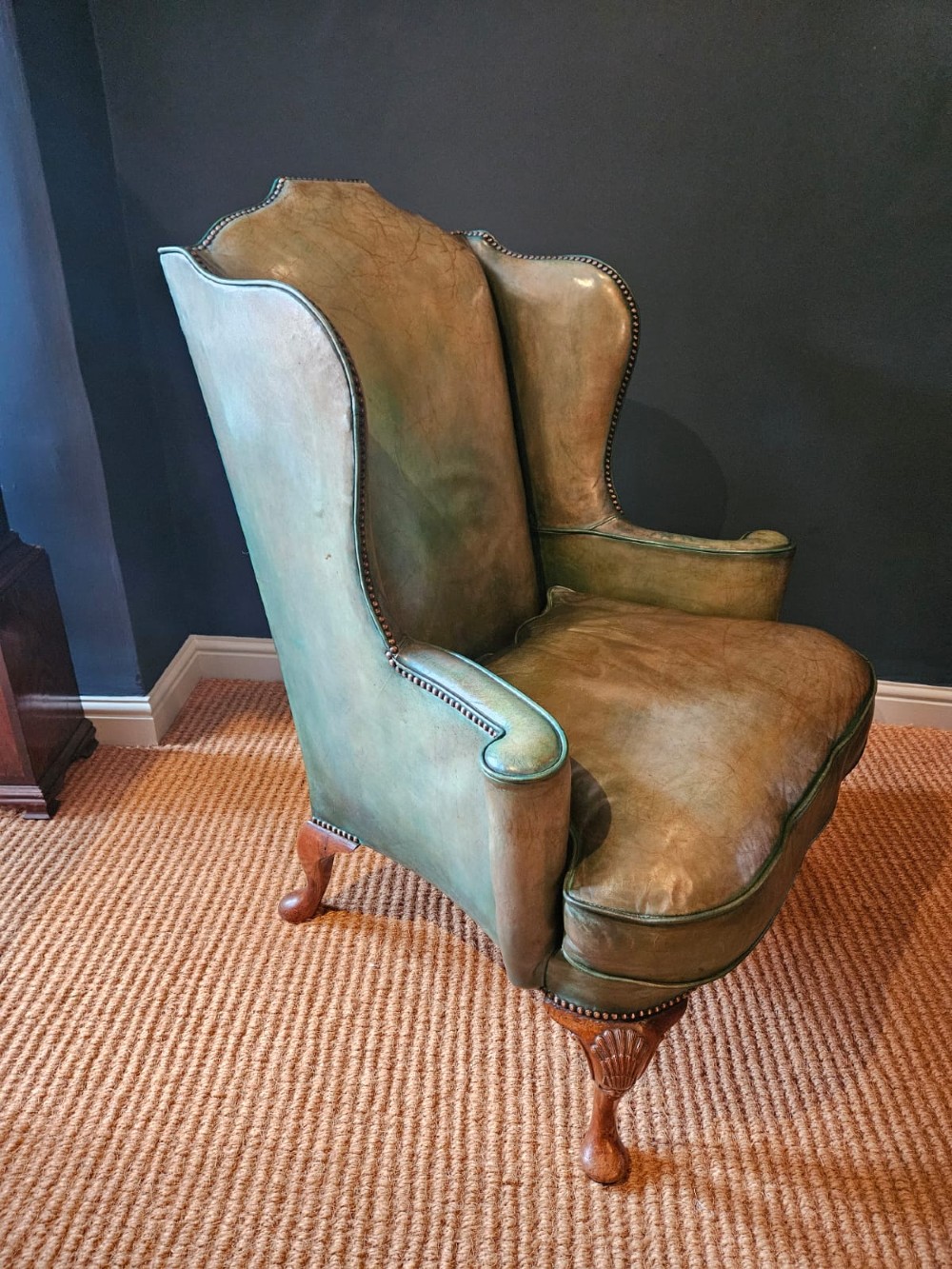 A George III wingback armchair in green leather upholstery featuring brass studding and carved walnut cabriole front legs. View VI
