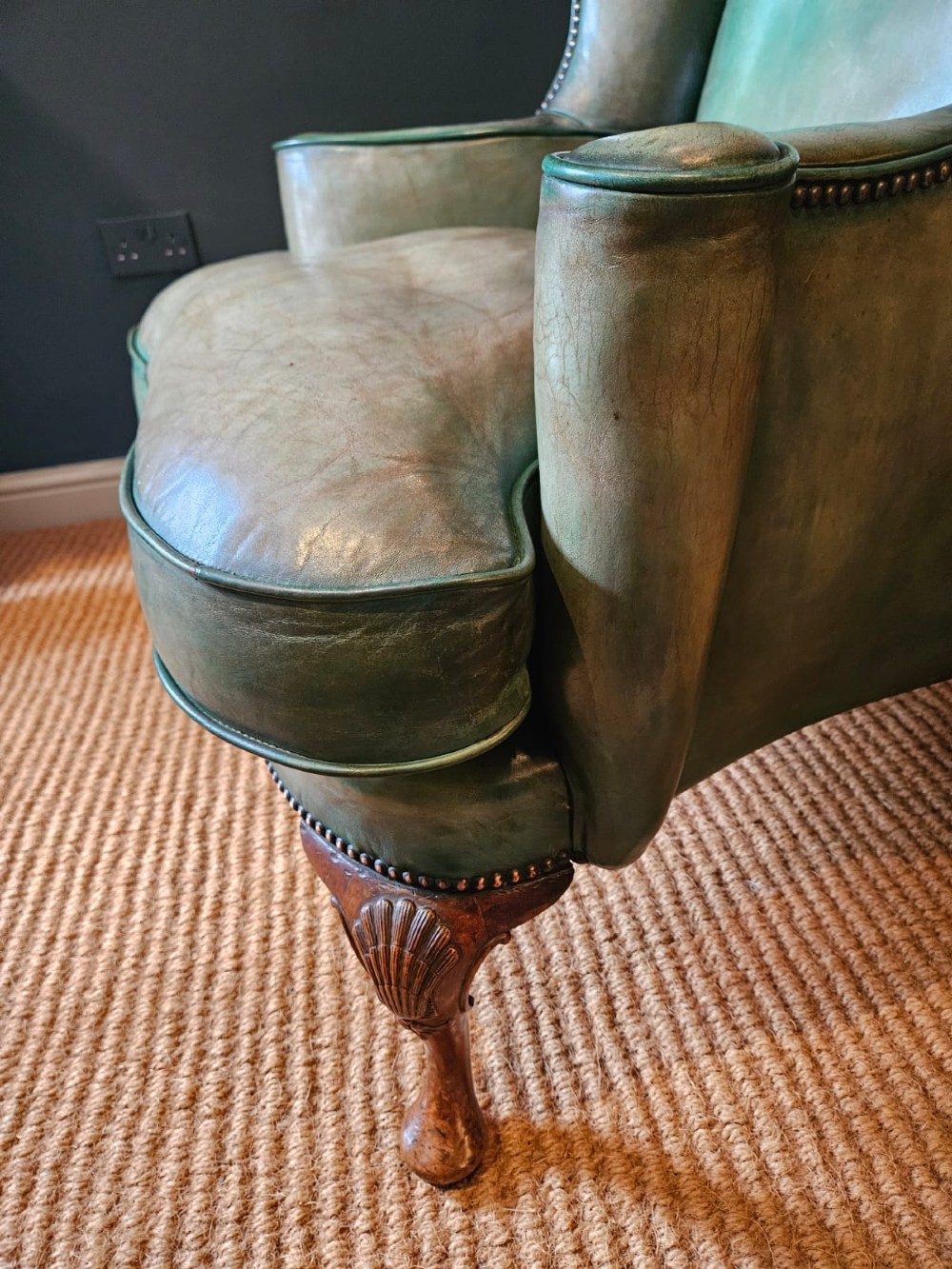 A George III wingback armchair in green leather upholstery featuring brass studding and carved walnut cabriole front legs. View VII