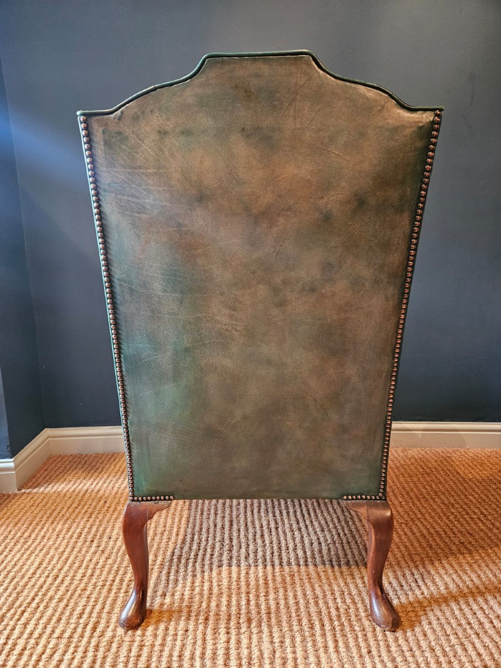 A George III wingback armchair in green leather upholstery featuring brass studding and carved walnut cabriole front legs. View VIII