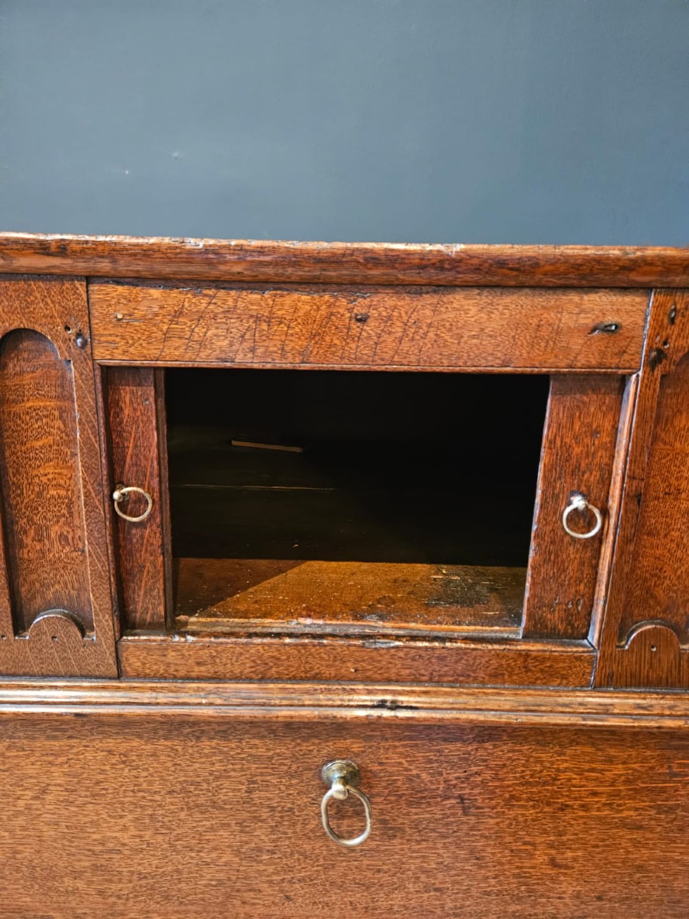 A George III dark oak nightstand featuring a tray top gallery, central cupboard doors flanked by carved arch panels, a lower drawer, and brass ring handles. View IV
