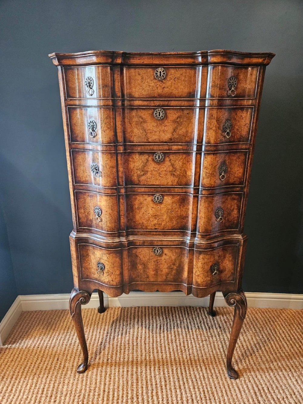 An Edwardian burr walnut chest on stand featuring a serpentine front, ornate brass handles, and slender cabriole legs.