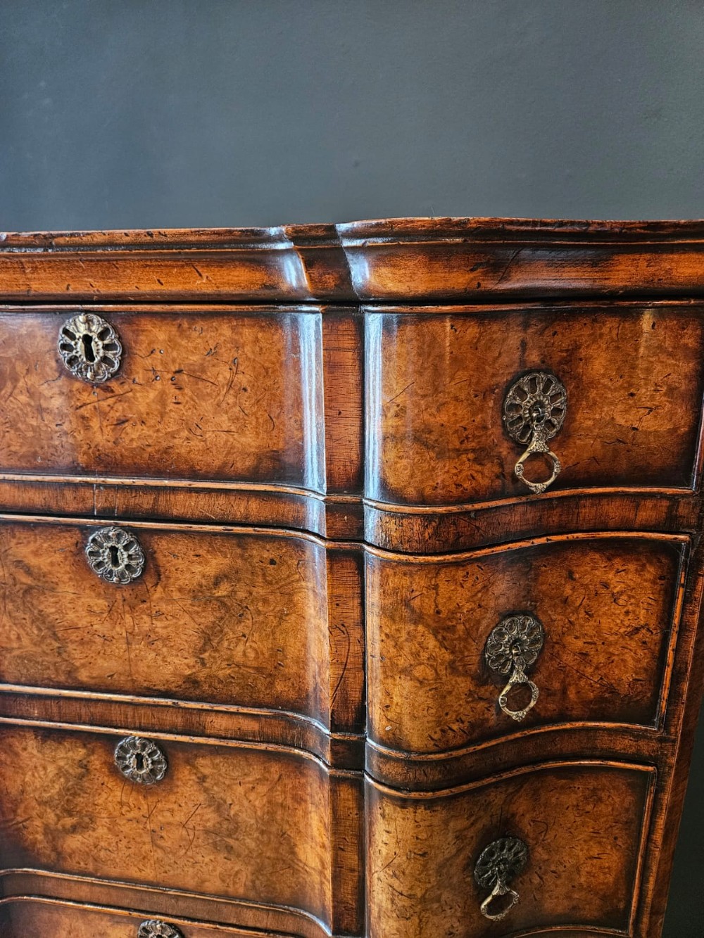 An Edwardian burr walnut chest on stand featuring a serpentine front, ornate brass handles, and slender cabriole legs. View II