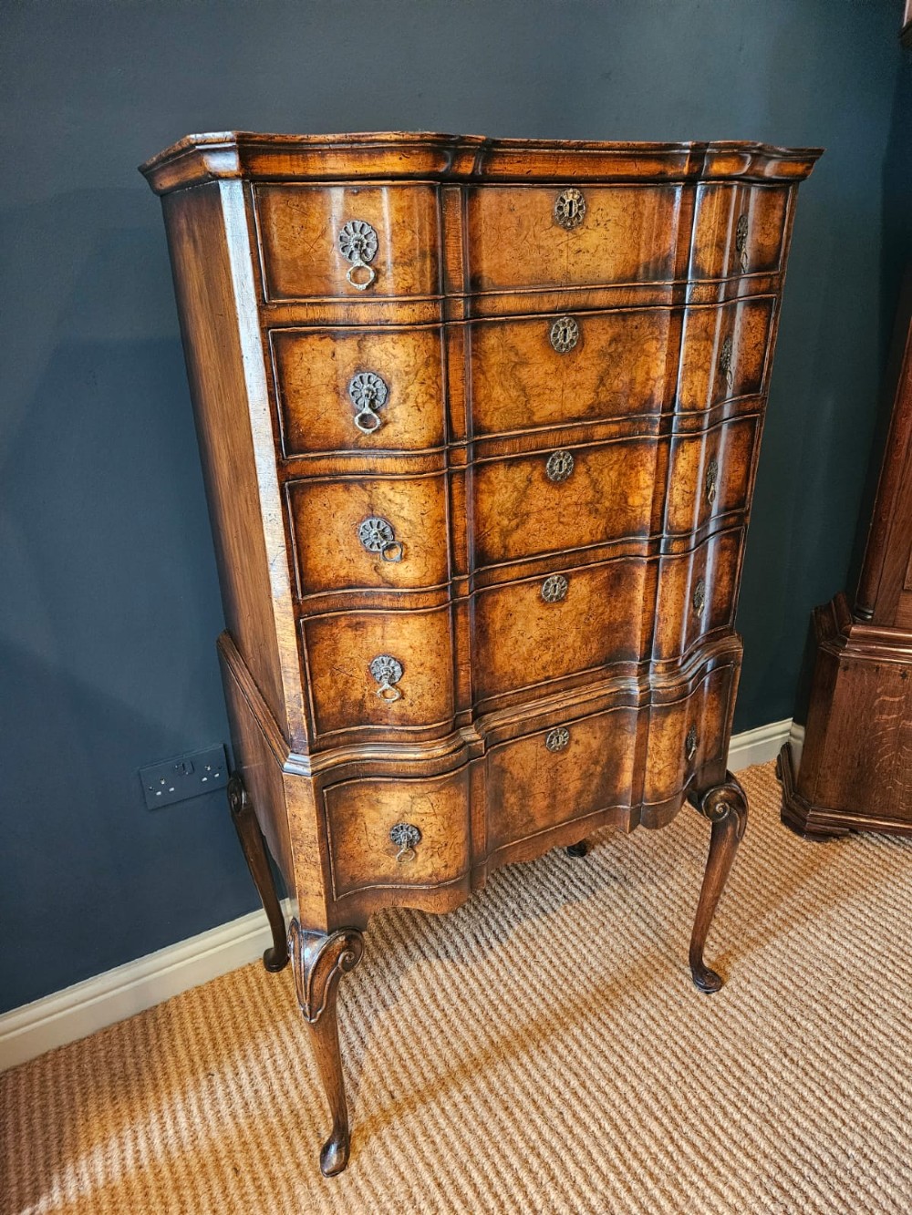 An Edwardian burr walnut chest on stand featuring a serpentine front, ornate brass handles, and slender cabriole legs. View IV