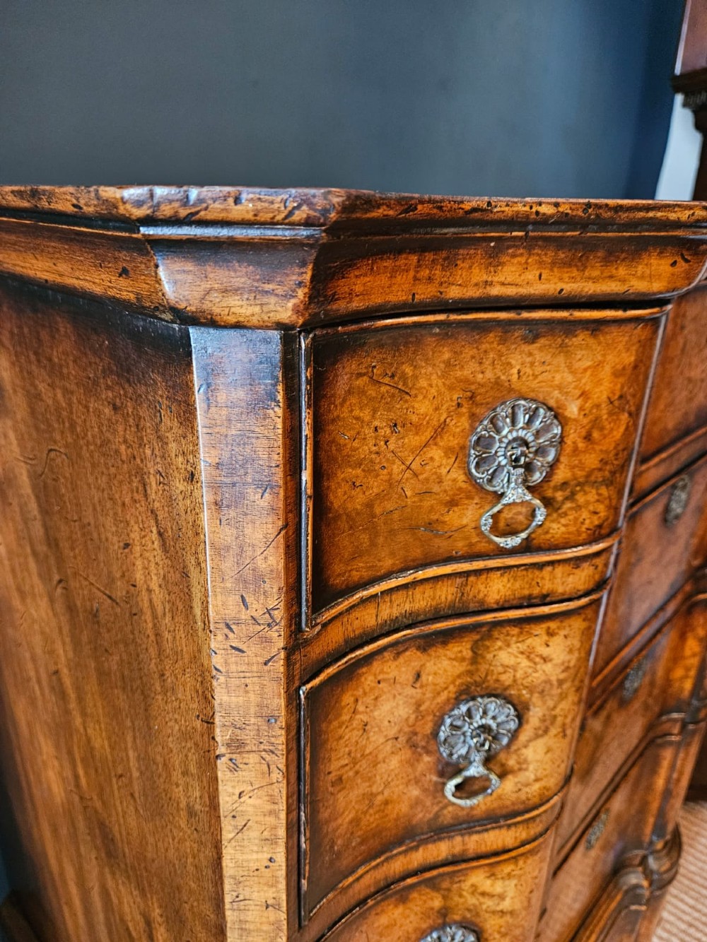 An Edwardian burr walnut chest on stand featuring a serpentine front, ornate brass handles, and slender cabriole legs. View VII