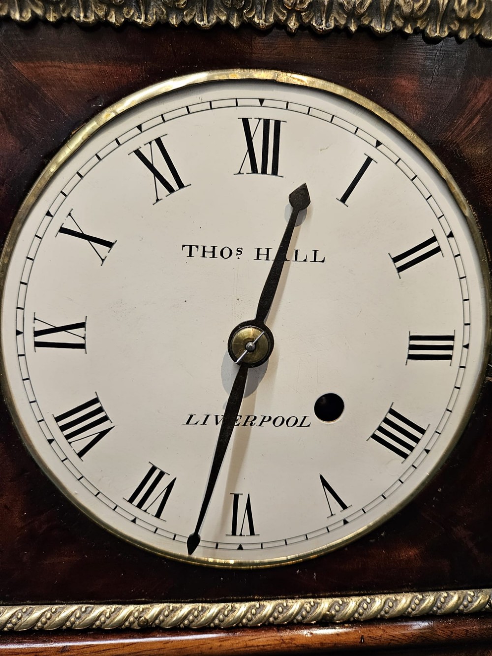 A small Regency period mahogany bracket clock featuring brass inlay, side grilles, a circular dial with Roman numerals, and a carved fluted finial. View VII