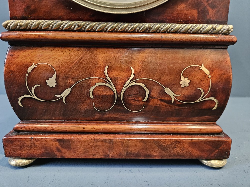 A small Regency period mahogany bracket clock featuring brass inlay, side grilles, a circular dial with Roman numerals, and a carved fluted finial. View VIII