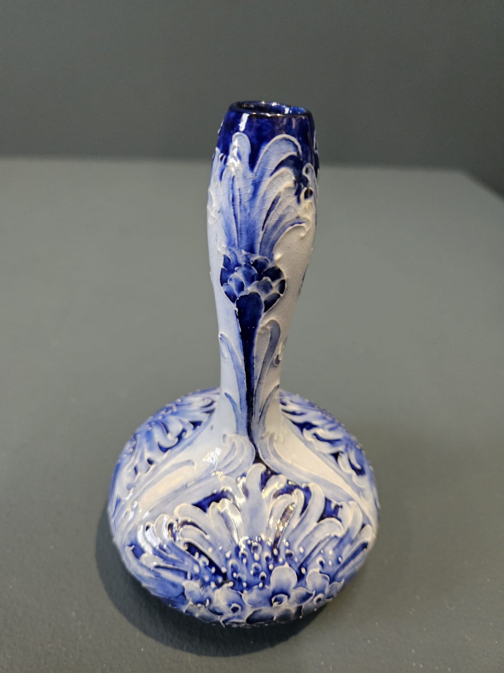 An Art Nouveau ceramic vase featuring a bulbous base, slender elongated neck, and cobalt blue tube-lined cornflower motif on a pale ground. View II