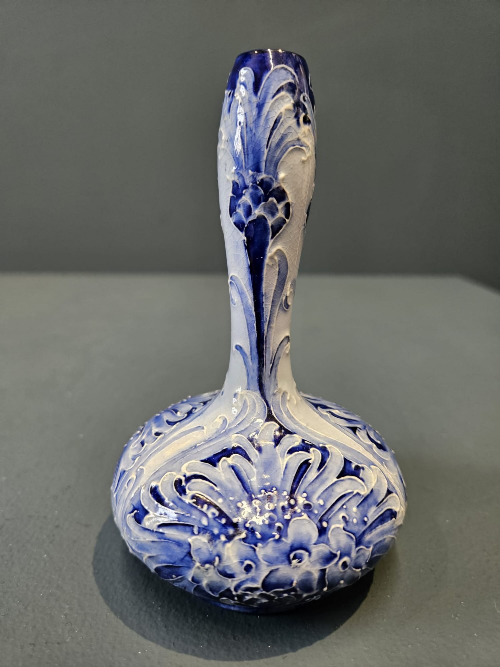 An Art Nouveau ceramic vase featuring a bulbous base, slender elongated neck, and cobalt blue tube-lined cornflower motif on a pale ground. View IV