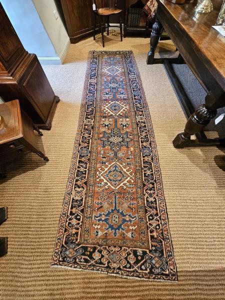 A long hand-knotted wool runner rug featuring central geometric medallion motifs in terracotta brown, indigo blue, and cream with a decorated navy border. View II