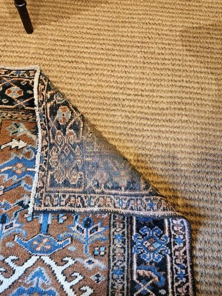 A long hand-knotted wool runner rug featuring central geometric medallion motifs in terracotta brown, indigo blue, and cream with a decorated navy border. View IV