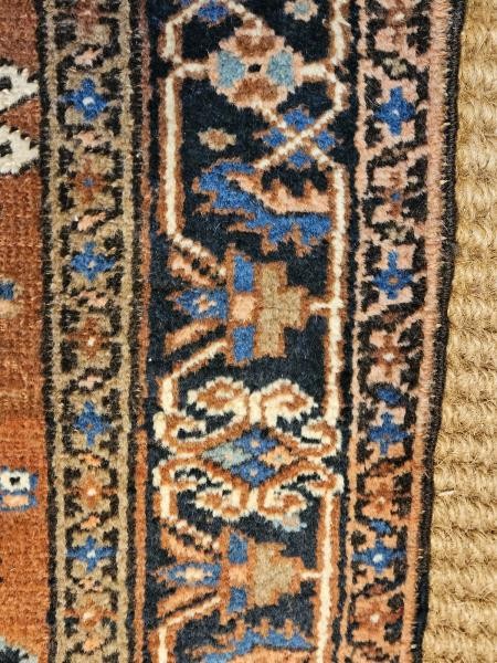A long hand-knotted wool runner rug featuring central geometric medallion motifs in terracotta brown, indigo blue, and cream with a decorated navy border. View VI