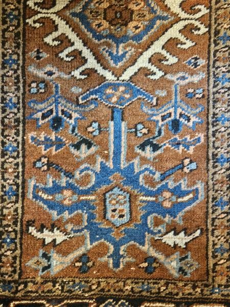 A long hand-knotted wool runner rug featuring central geometric medallion motifs in terracotta brown, indigo blue, and cream with a decorated navy border. View VII