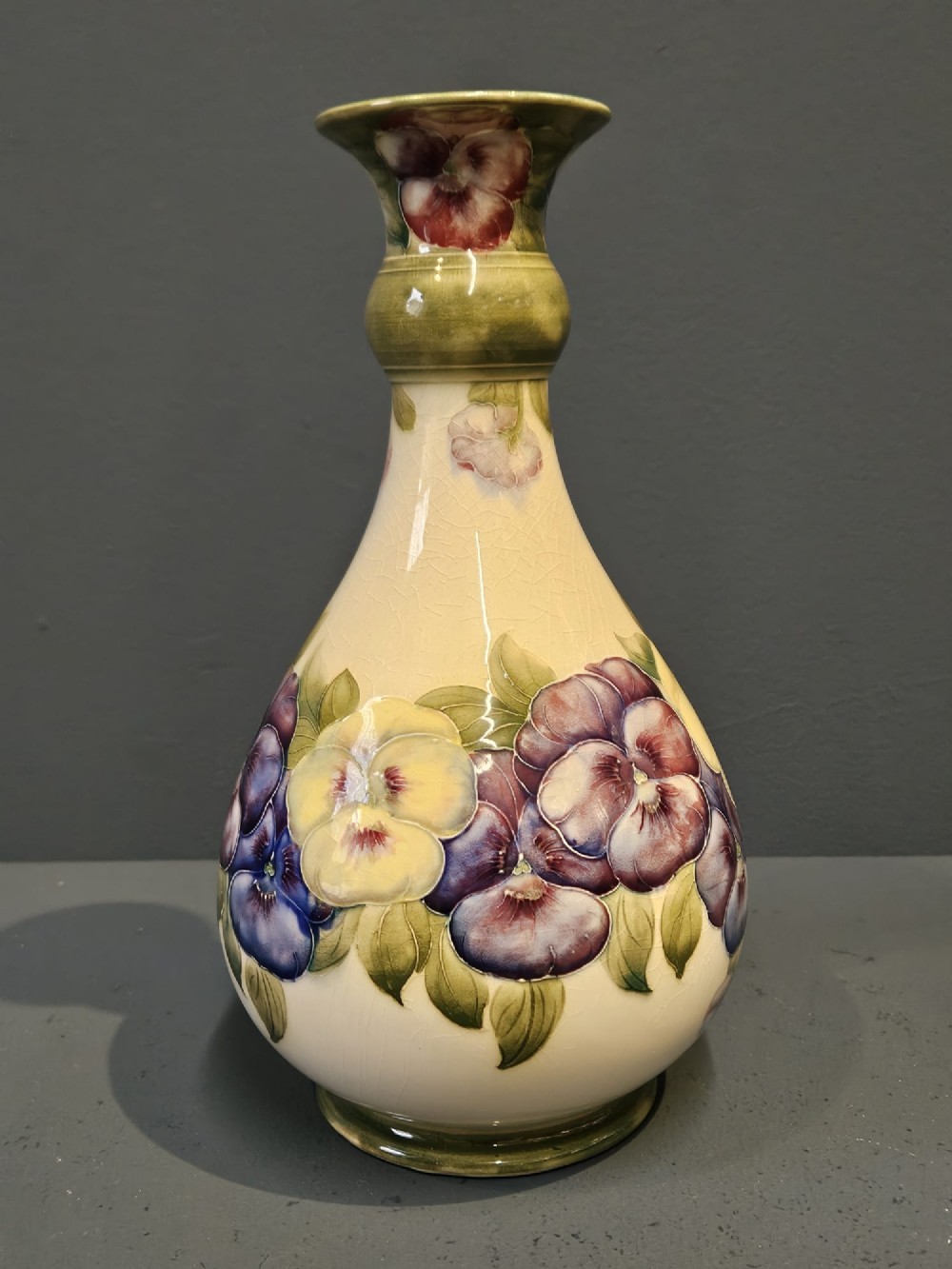 An Art Nouveau Macintyre Moorcroft earthenware vase featuring hand-painted tubelined pansy motifs on a cream ground with a green flared rim. View II