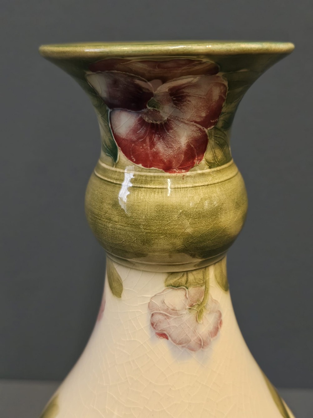 An Art Nouveau Macintyre Moorcroft earthenware vase featuring hand-painted tubelined pansy motifs on a cream ground with a green flared rim. View IV
