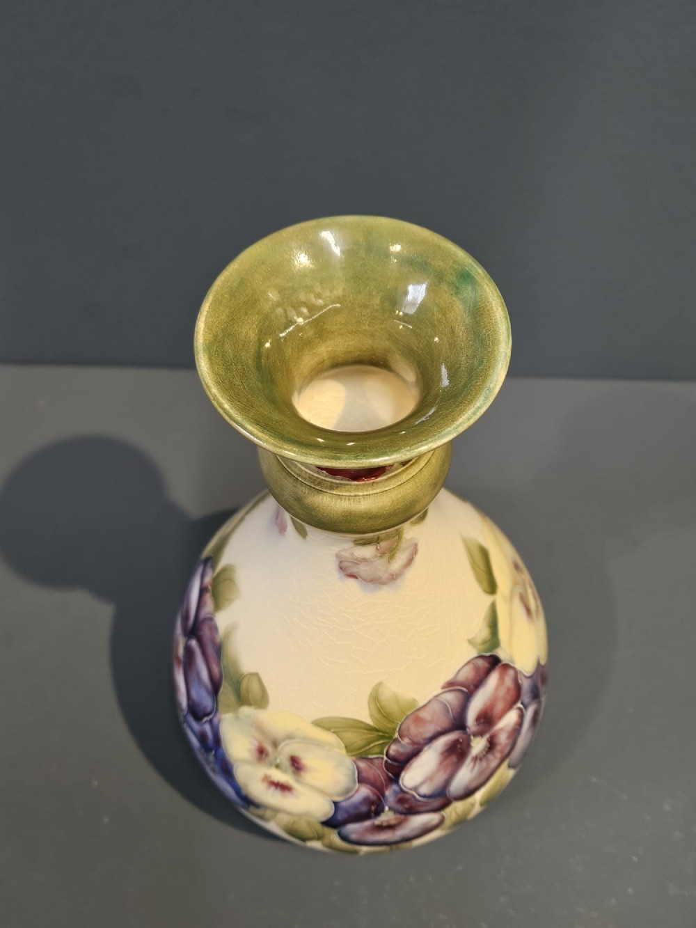 An Art Nouveau Macintyre Moorcroft earthenware vase featuring hand-painted tubelined pansy motifs on a cream ground with a green flared rim. View V