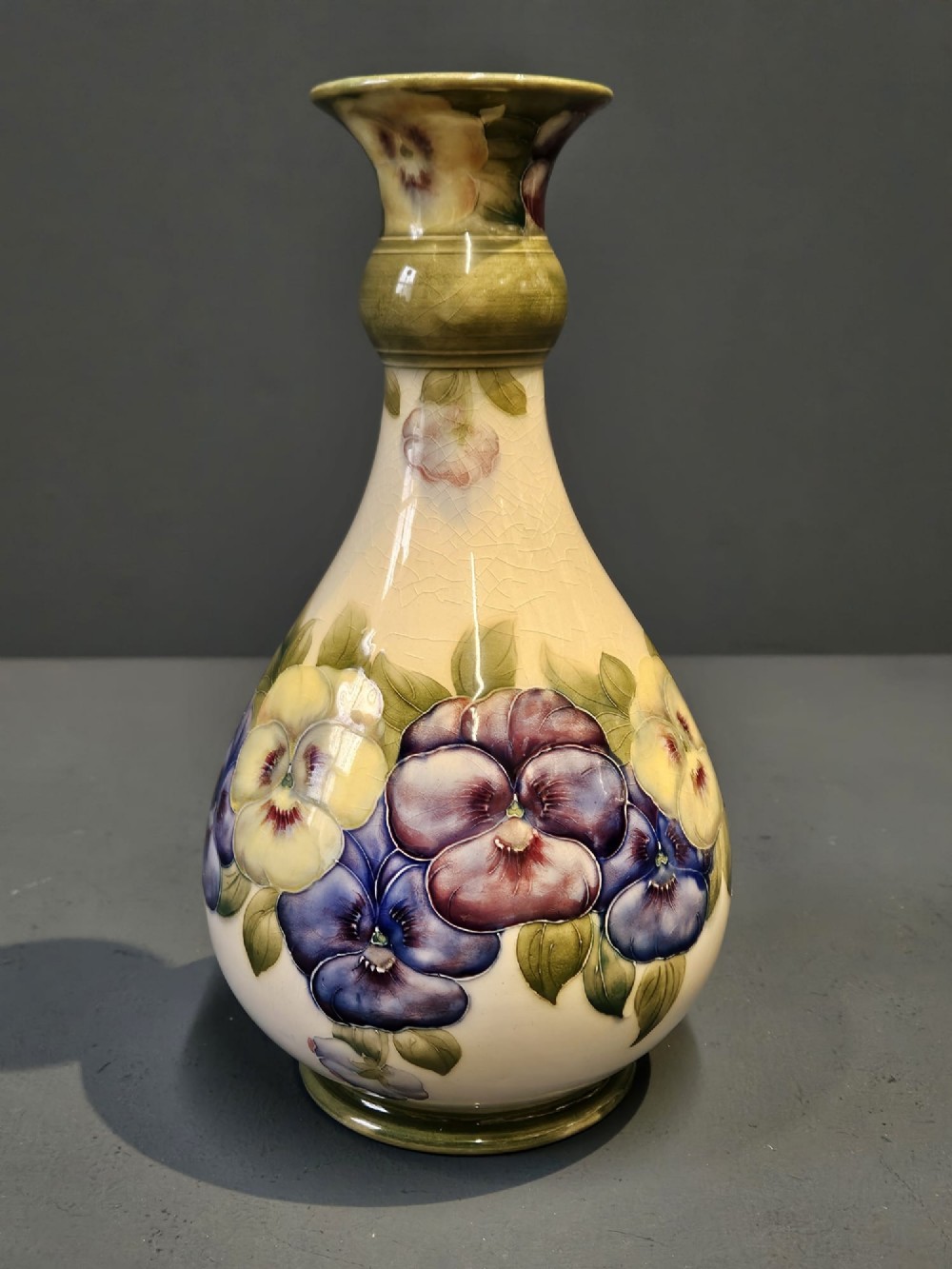 An Art Nouveau Macintyre Moorcroft earthenware vase featuring hand-painted tubelined pansy motifs on a cream ground with a green flared rim. View VI