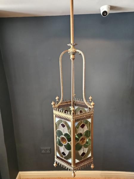 A vertical hexagonal brass hanging lantern featuring stained leaded glass panels with green, purple, and amber floral motifs. View II