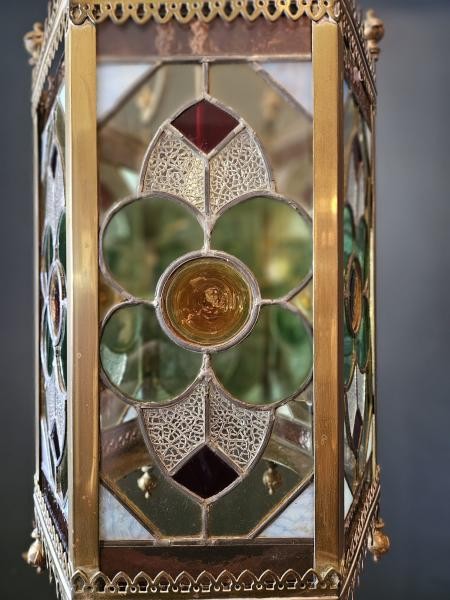 A vertical hexagonal brass hanging lantern featuring stained leaded glass panels with green, purple, and amber floral motifs. View V