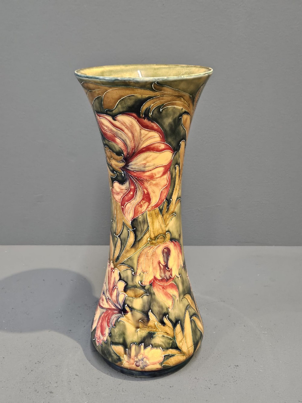 A tall flared ceramic vase decorated with tubelined Art Nouveau floral patterns in shades of red, ochre, and earthy green.