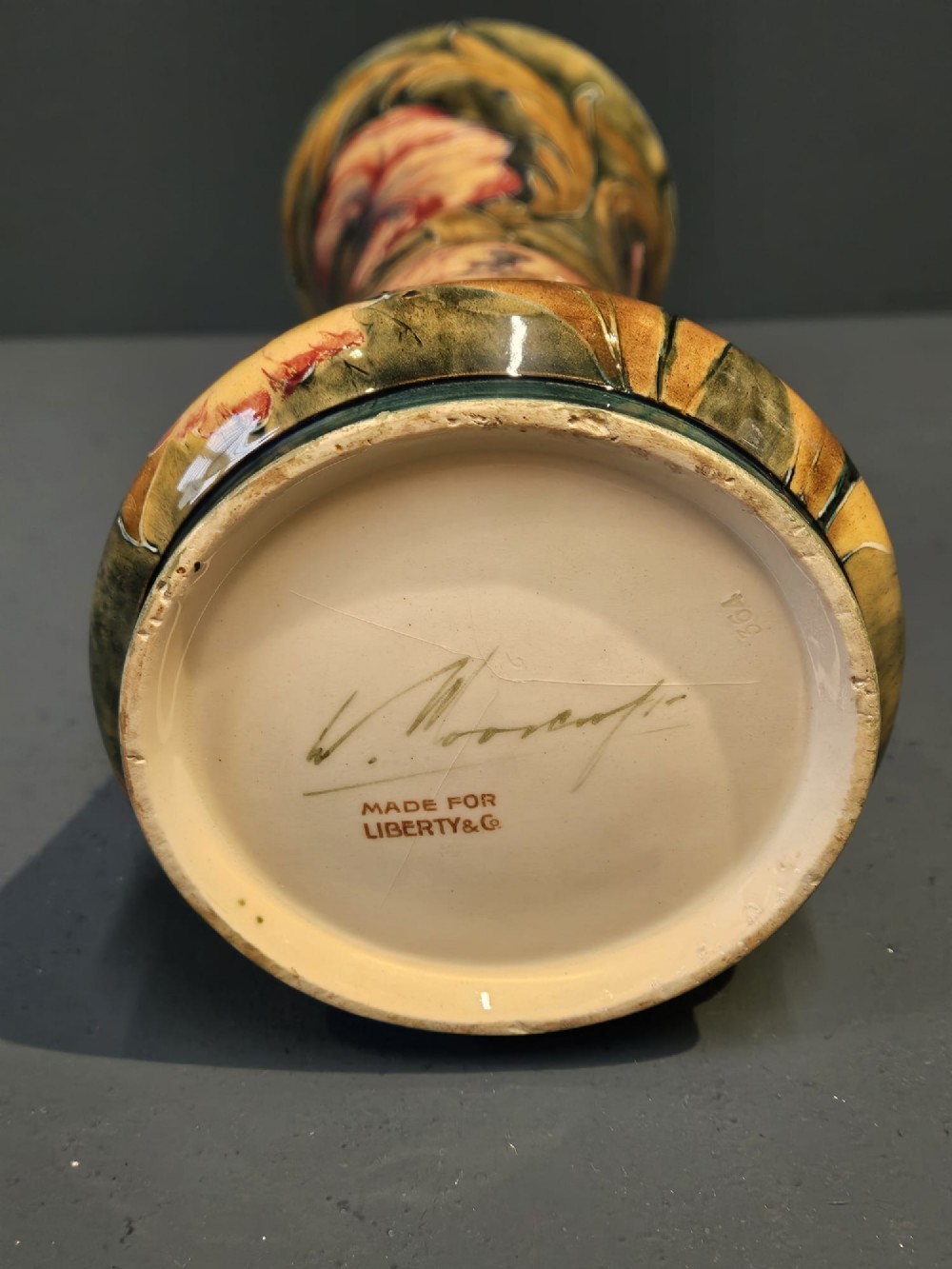 A tall flared ceramic vase decorated with tubelined Art Nouveau floral patterns in shades of red, ochre, and earthy green. View II