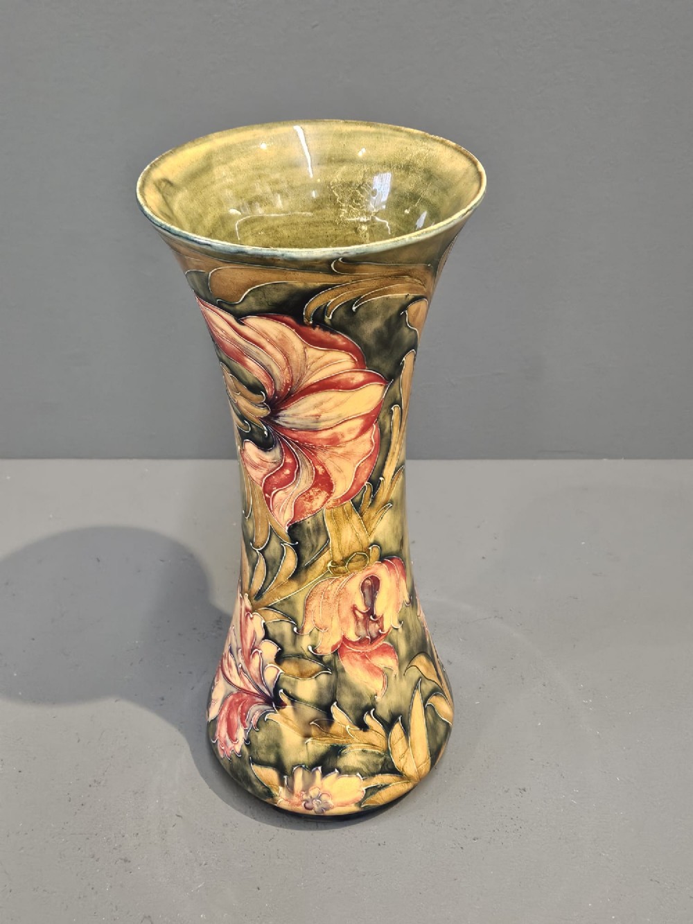 A tall flared ceramic vase decorated with tubelined Art Nouveau floral patterns in shades of red, ochre, and earthy green. View III