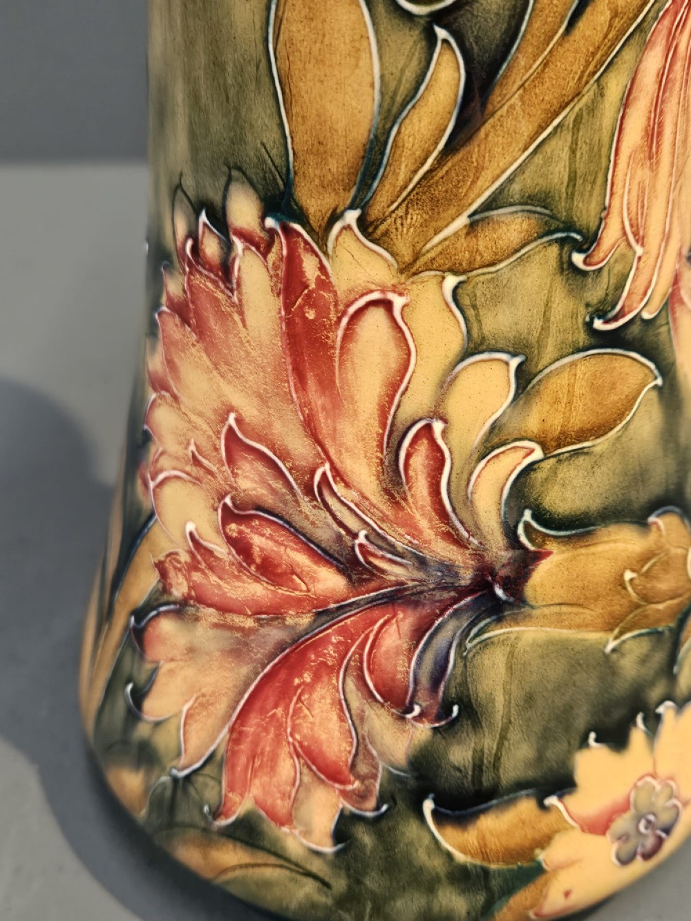 A tall flared ceramic vase decorated with tubelined Art Nouveau floral patterns in shades of red, ochre, and earthy green. View IV