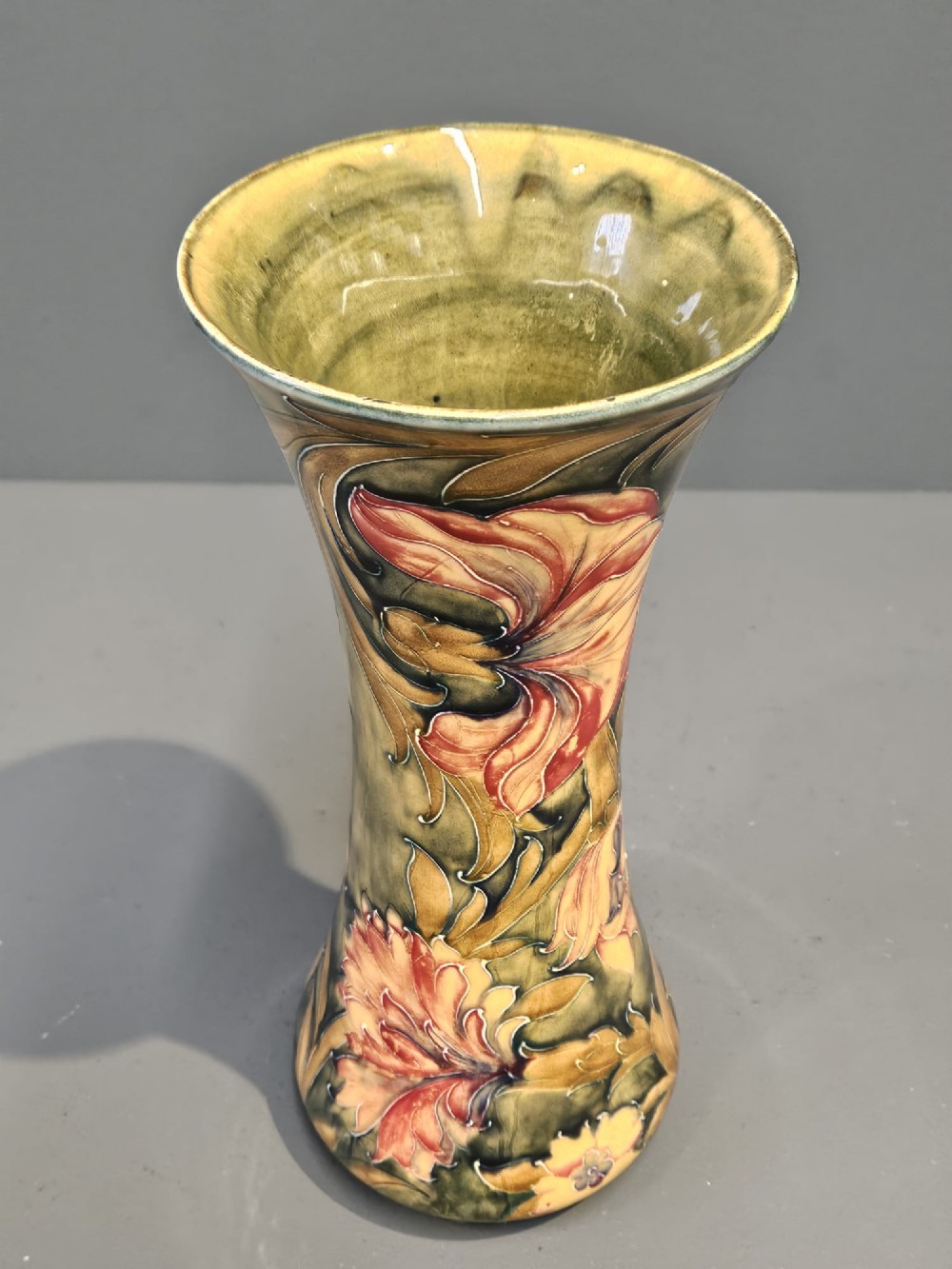 A tall flared ceramic vase decorated with tubelined Art Nouveau floral patterns in shades of red, ochre, and earthy green. View V
