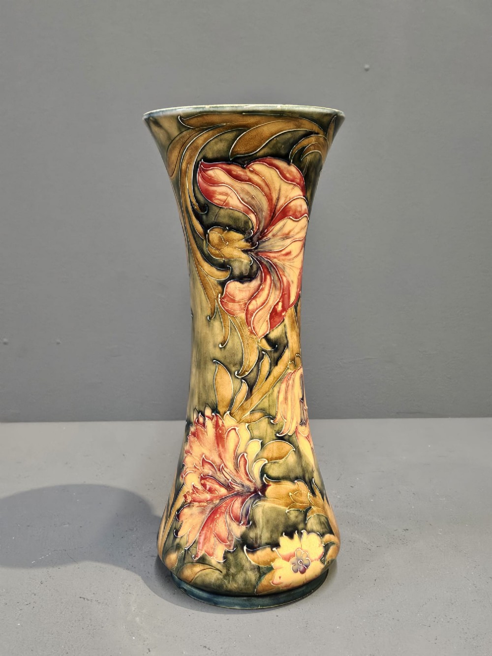 A tall flared ceramic vase decorated with tubelined Art Nouveau floral patterns in shades of red, ochre, and earthy green. View VI