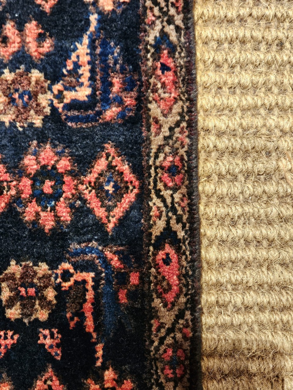A long hand-knotted wool runner rug featuring repeating geometric diamond patterns in red, cream, and terracotta on a dark navy background with fringe edges. View V