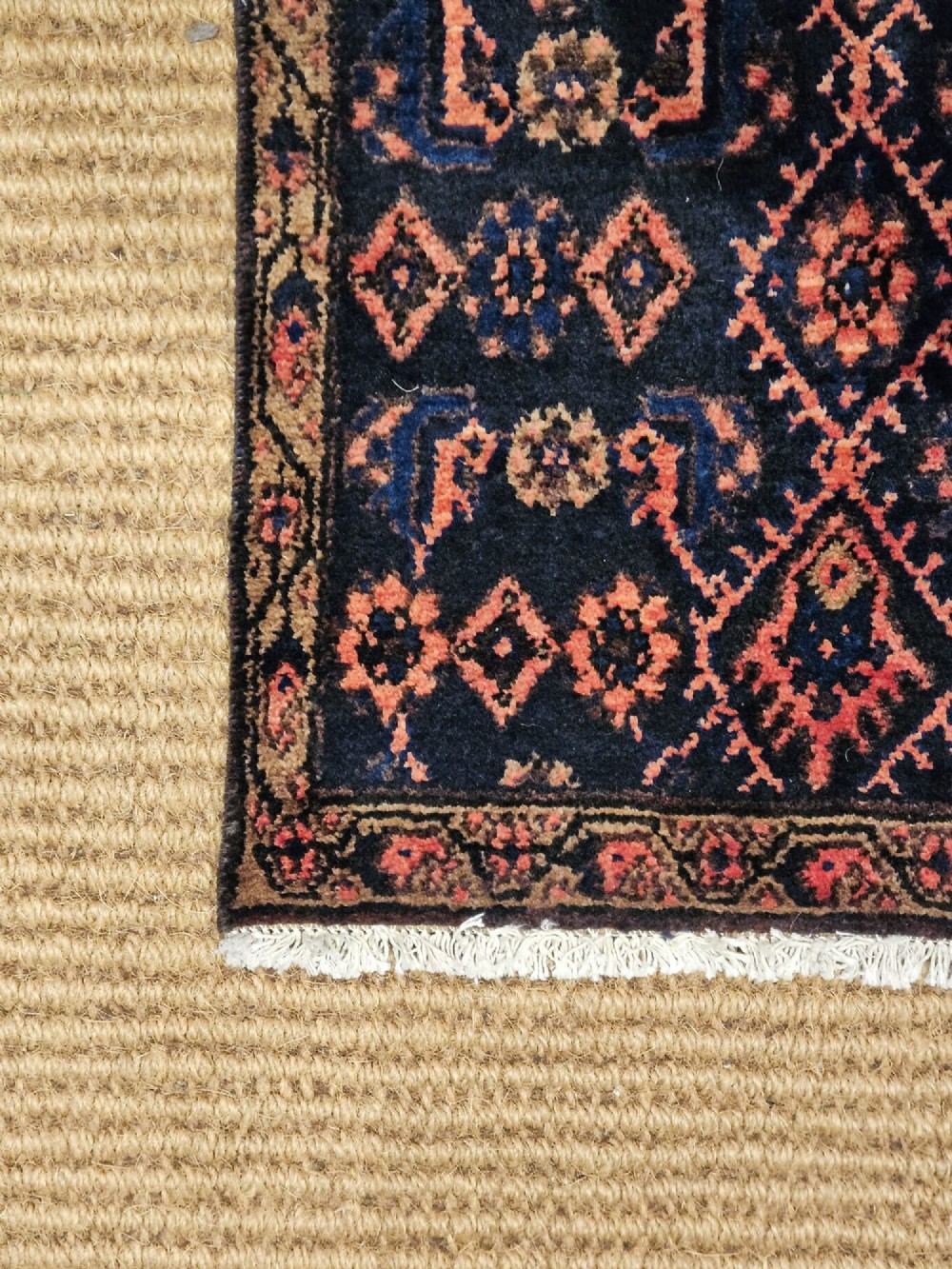 A long hand-knotted wool runner rug featuring repeating geometric diamond patterns in red, cream, and terracotta on a dark navy background with fringe edges. View VII