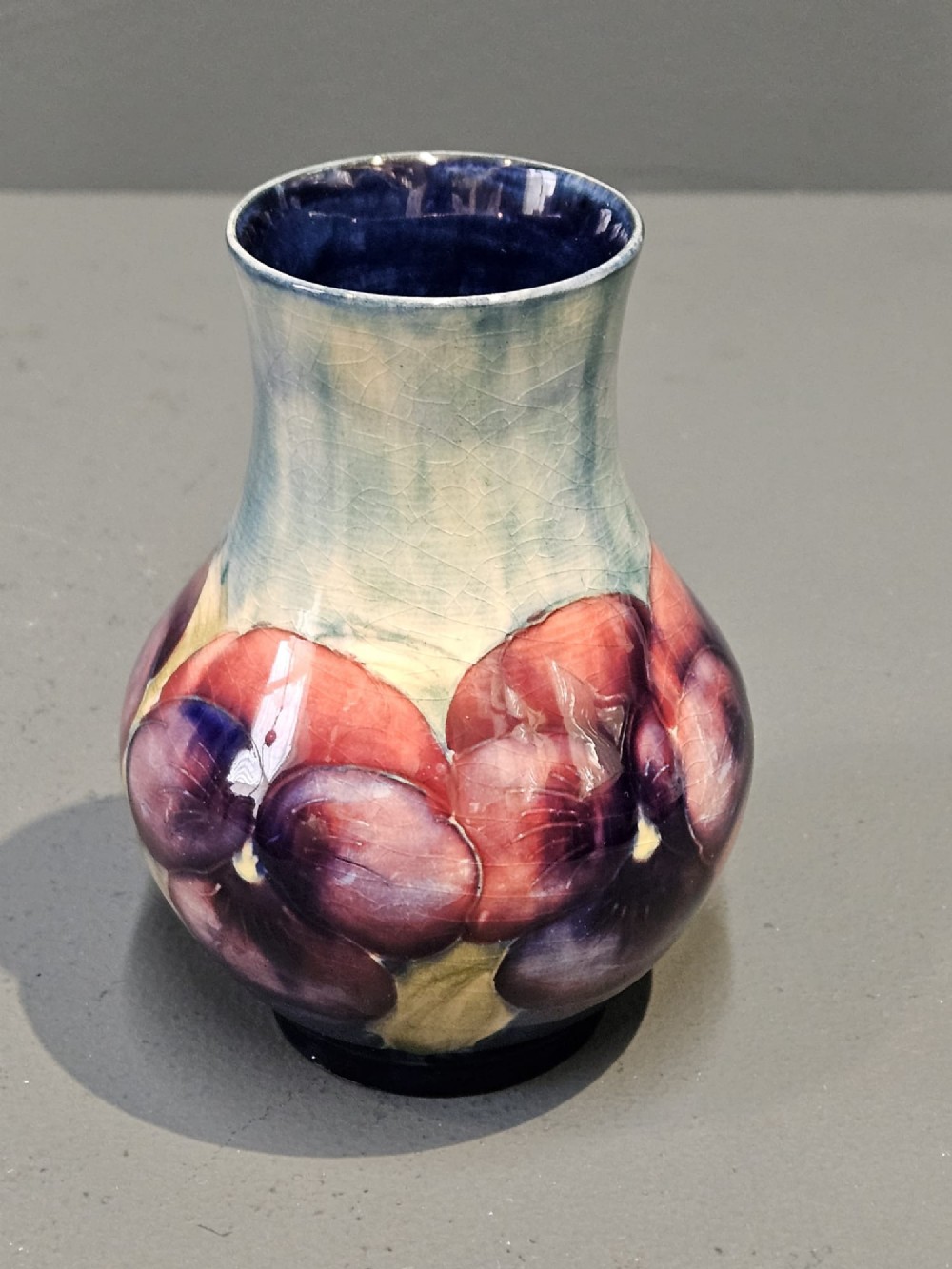 A Moorcroft earthenware vase featuring a bulbous body and flared neck decorated with hand-painted tubelined purple and wine-red pansies beneath a pale blue glaze. View II