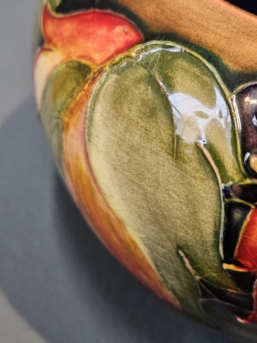 A small round earthenware vase decorated with tubelined autumn leaves and berries in yellow, green, and red against a dark flambe glaze. View III