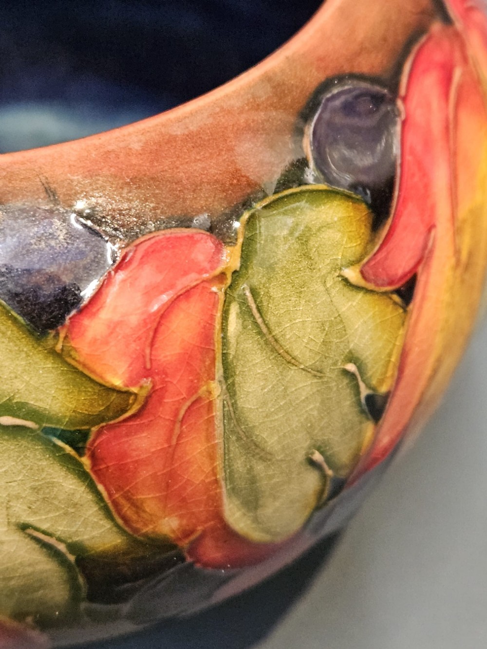 A small round earthenware vase decorated with tubelined autumn leaves and berries in yellow, green, and red against a dark flambe glaze. View IV