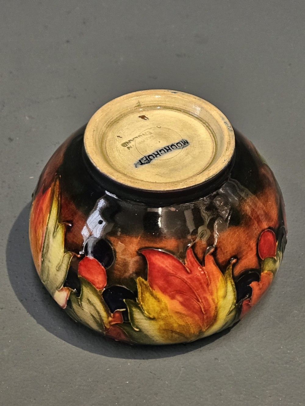 A small round earthenware vase decorated with tubelined autumn leaves and berries in yellow, green, and red against a dark flambe glaze. View VII