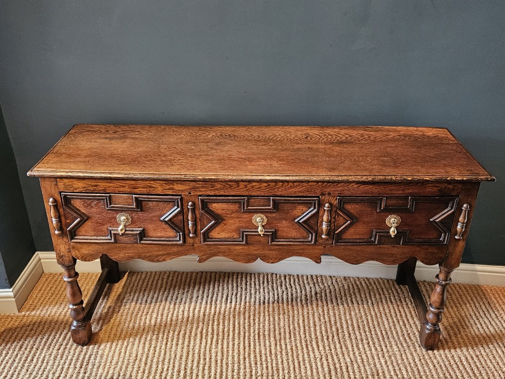 An early 18th-century George I oak dresser featuring three drawers with geometric mitred mouldings, brass drop handles, a scalloped apron, and turned legs. View II