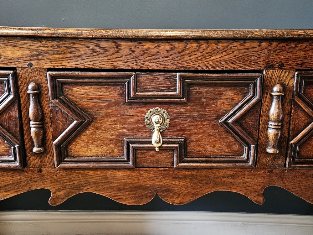 An early 18th-century George I oak dresser featuring three drawers with geometric mitred mouldings, brass drop handles, a scalloped apron, and turned legs. View III