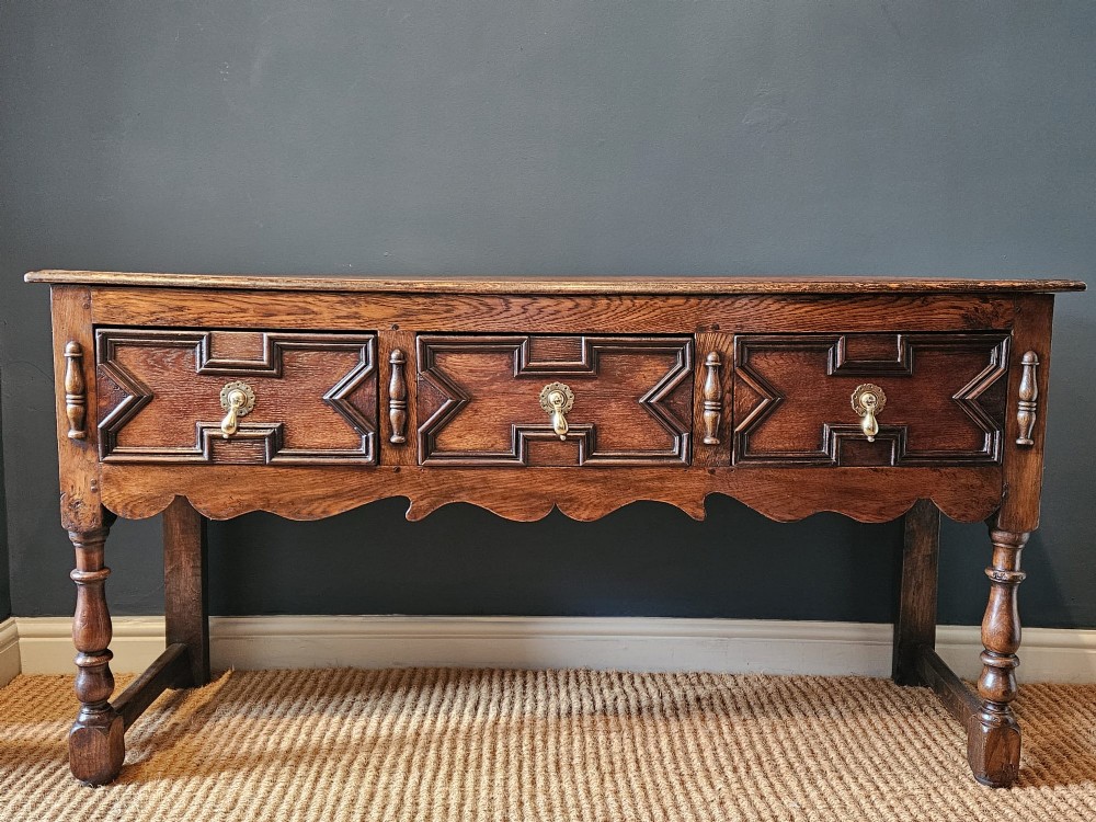An early 18th-century George I oak dresser featuring three drawers with geometric mitred mouldings, brass drop handles, a scalloped apron, and turned legs. View IV