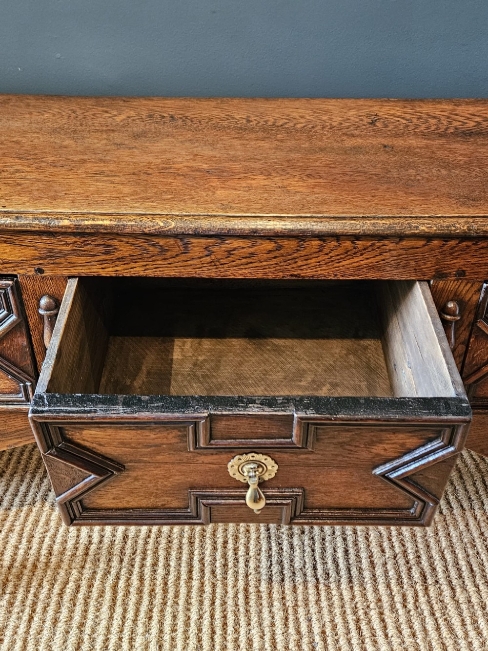 An early 18th-century George I oak dresser featuring three drawers with geometric mitred mouldings, brass drop handles, a scalloped apron, and turned legs. View V