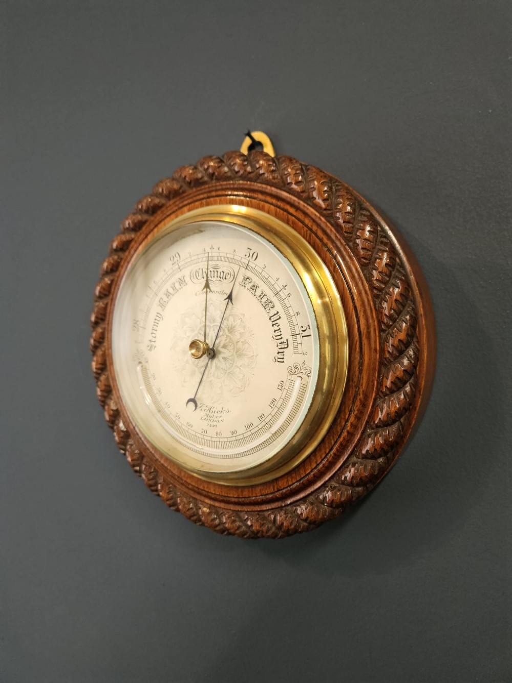 A circular Victorian aneroid barometer set in a carved oak rope-twist frame with a silvered engraved dial and a brass bezel. View II