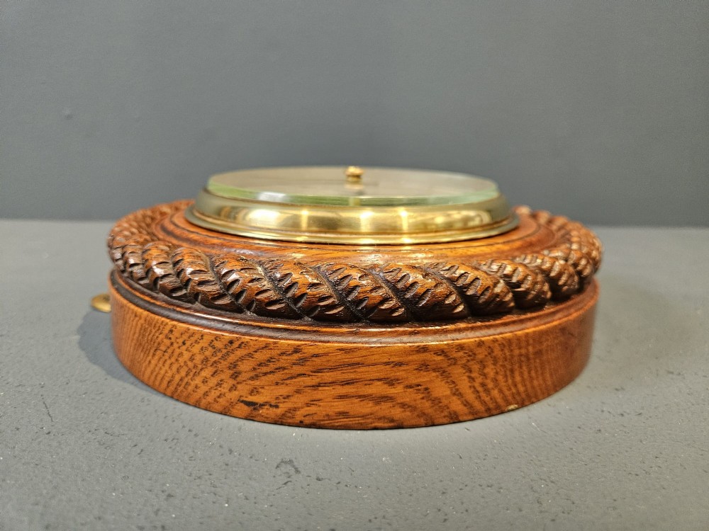A circular Victorian aneroid barometer set in a carved oak rope-twist frame with a silvered engraved dial and a brass bezel. View V