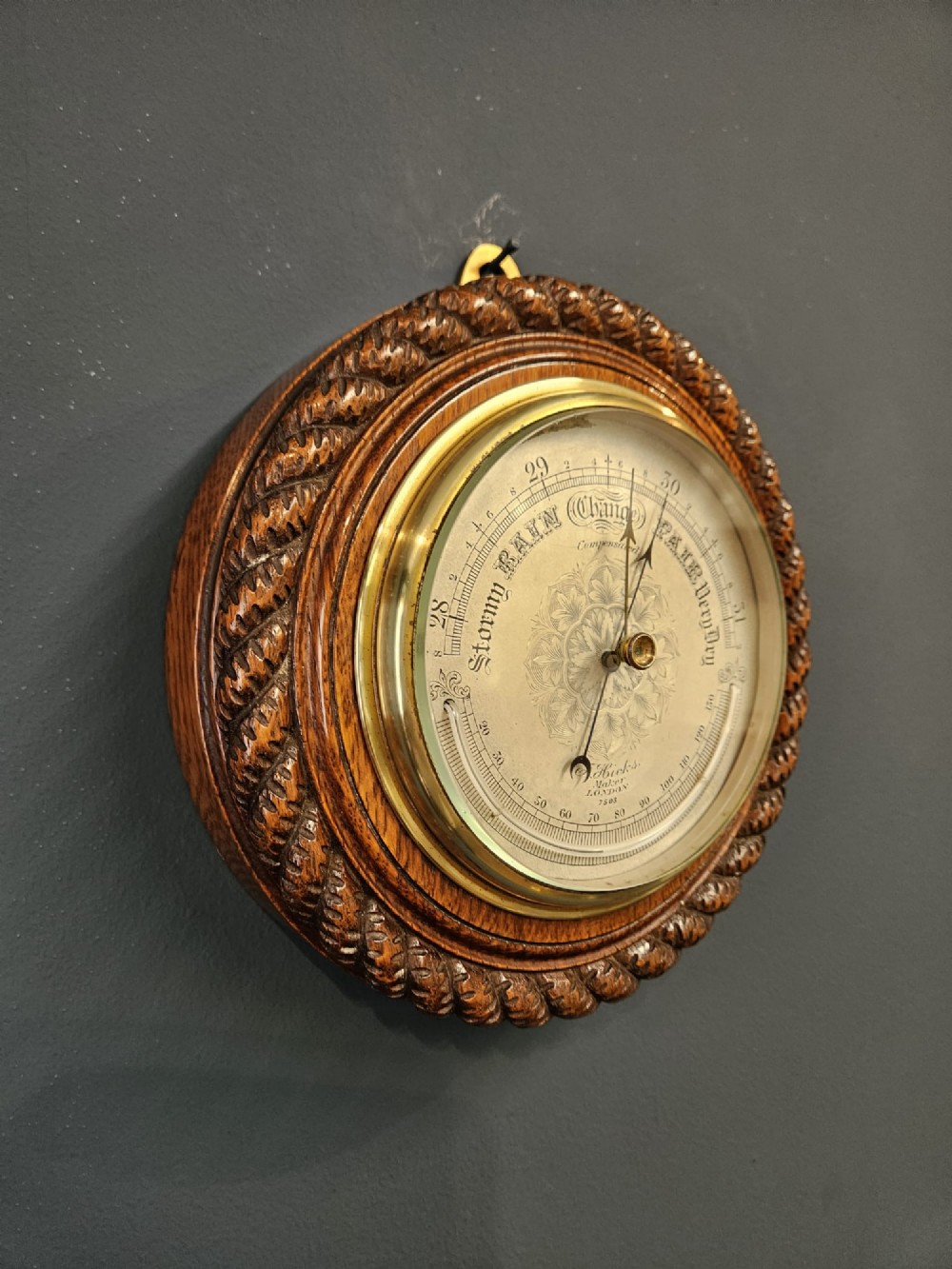 A circular Victorian aneroid barometer set in a carved oak rope-twist frame with a silvered engraved dial and a brass bezel. View VII