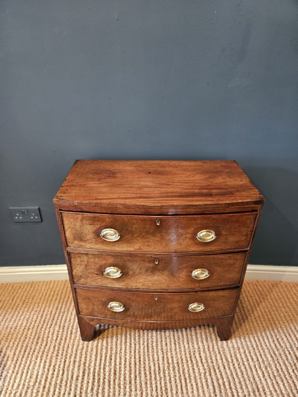 An early Victorian mahogany bow-fronted chest featuring three full-length drawers with oval brass handles and a curved lower apron. View IV