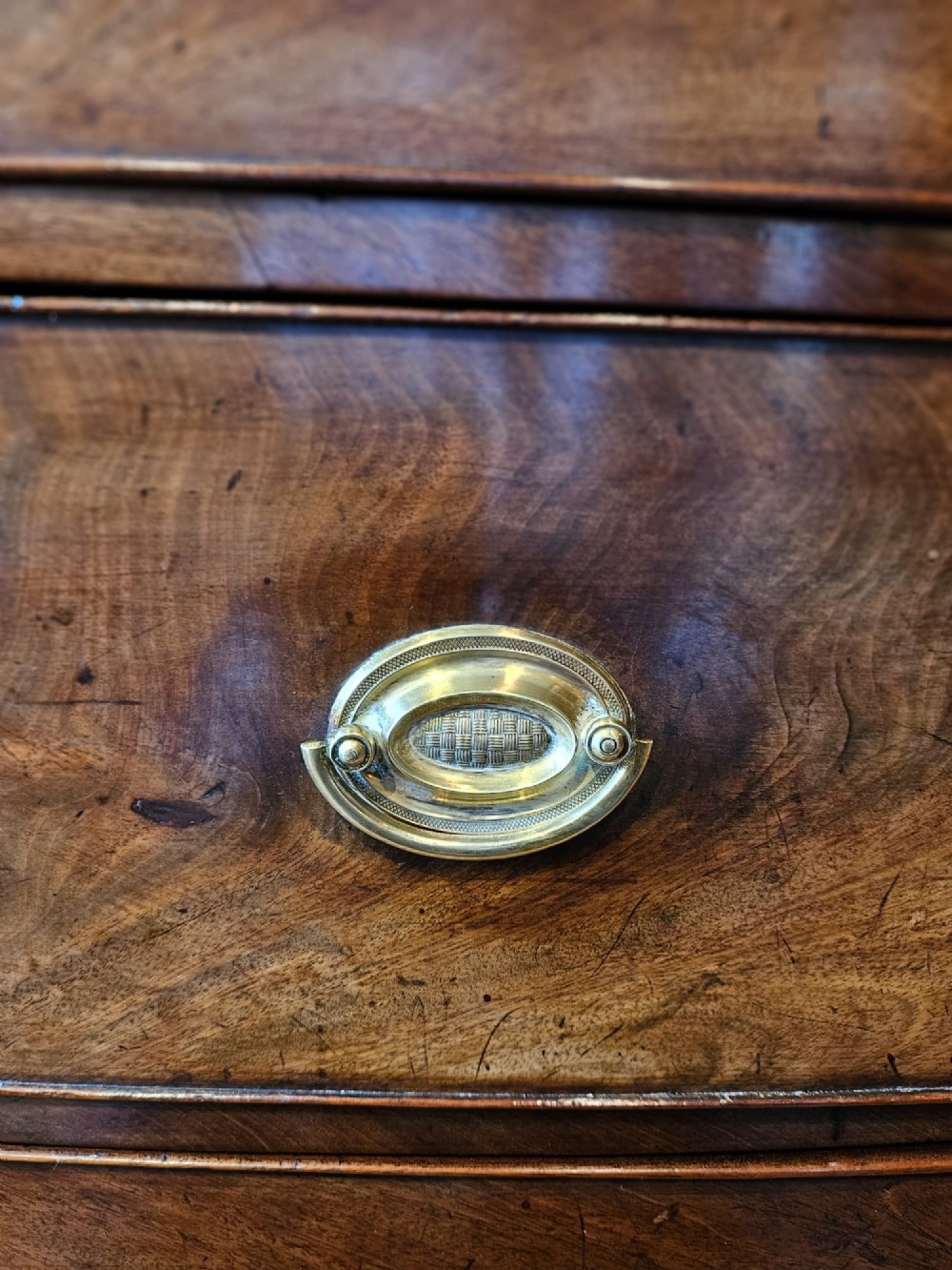 An early Victorian mahogany bow-fronted chest featuring three full-length drawers with oval brass handles and a curved lower apron. View VI