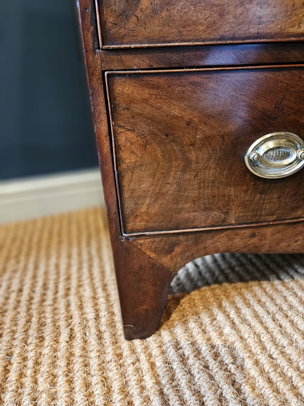 An early Victorian mahogany bow-fronted chest featuring three full-length drawers with oval brass handles and a curved lower apron. View VII