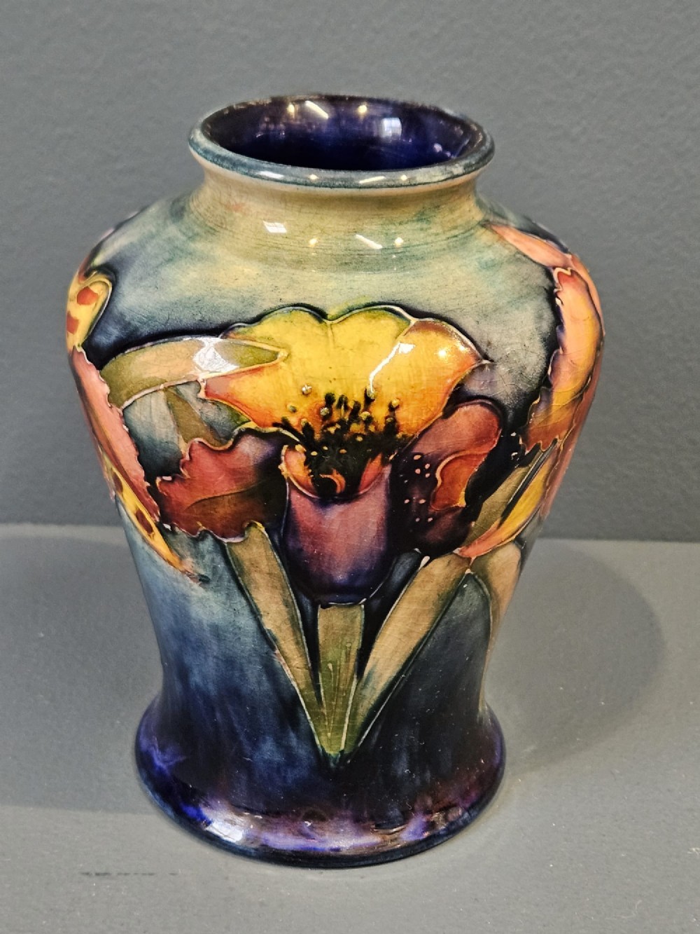 A glazed earthenware vase featuring tube-lined yellow and purple orchid motifs set against a rich blue and green flambe background.