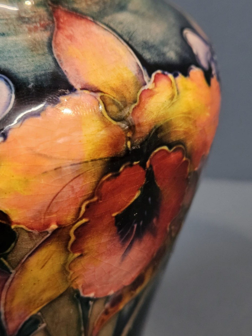 A glazed earthenware vase featuring tube-lined yellow and purple orchid motifs set against a rich blue and green flambe background. View II