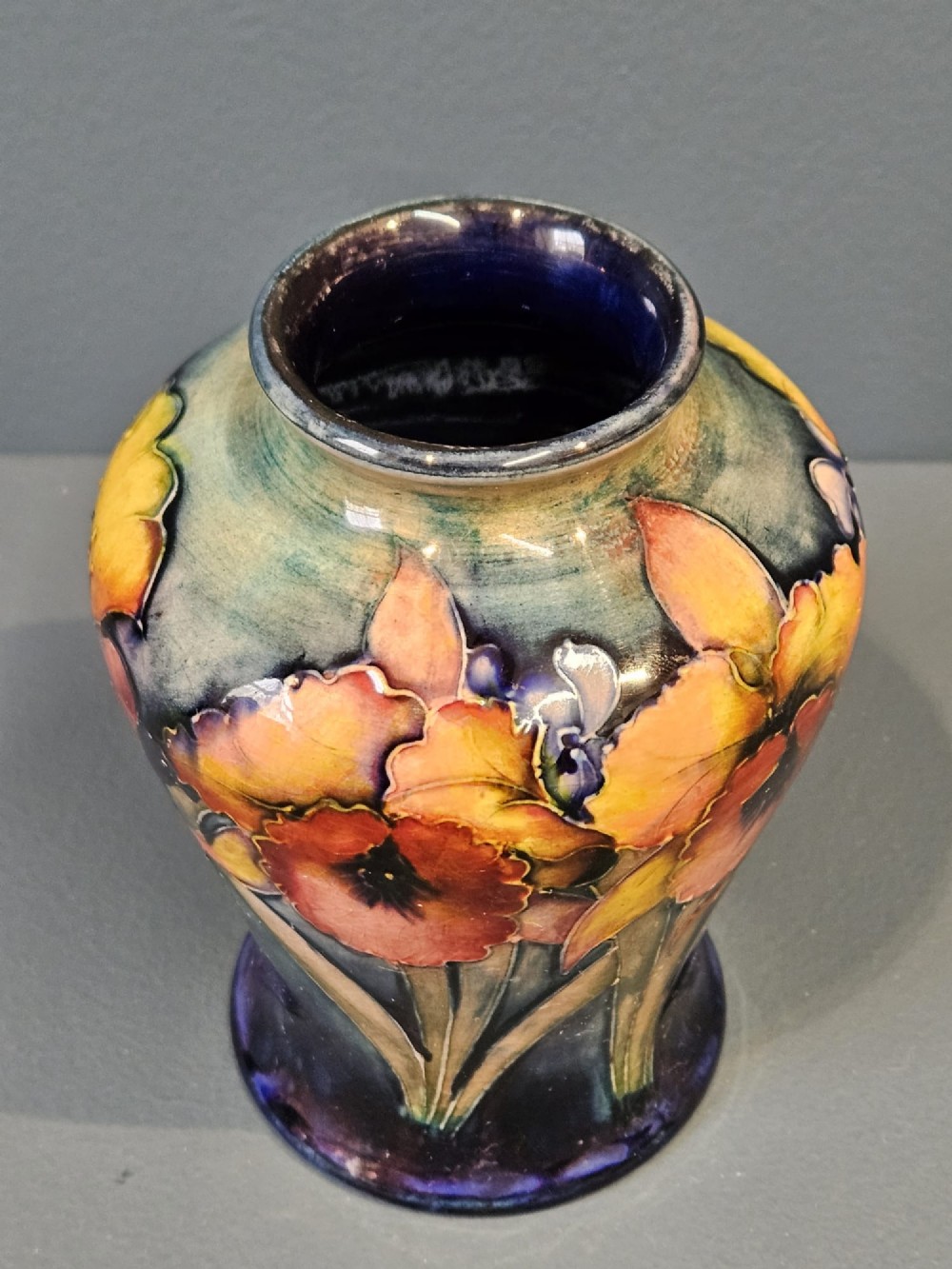 A glazed earthenware vase featuring tube-lined yellow and purple orchid motifs set against a rich blue and green flambe background. View III