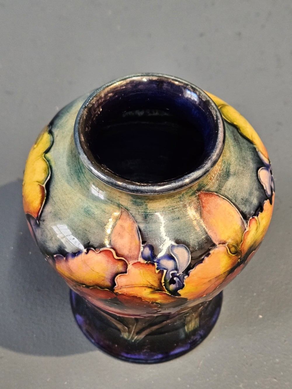 A glazed earthenware vase featuring tube-lined yellow and purple orchid motifs set against a rich blue and green flambe background. View V