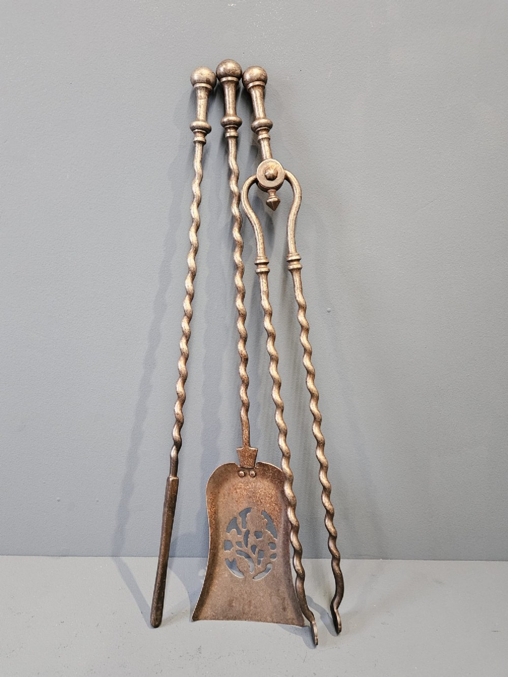 A set of three Georgian steel fire irons featuring barley twist shafts, turned urn finials, and a pierced decorative shovel blade.