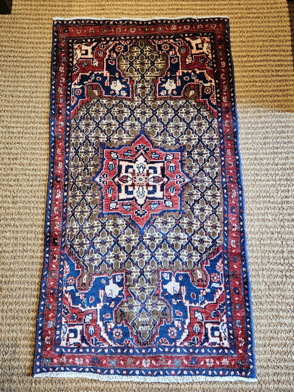 A small rectangular hand-knotted wool rug featuring a central star medallion, geometric lattice field, and deep red and blue borders.